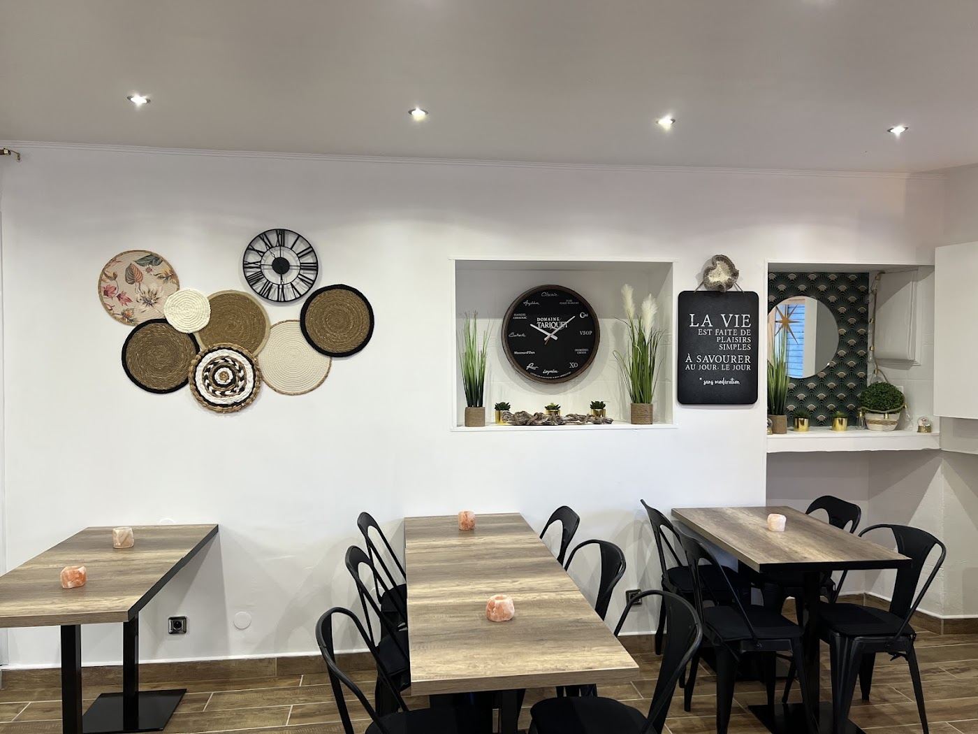 Salle claire du Coffee de France : tables en bois, chaises noires et décor mural d’assiettes et d’horloges.