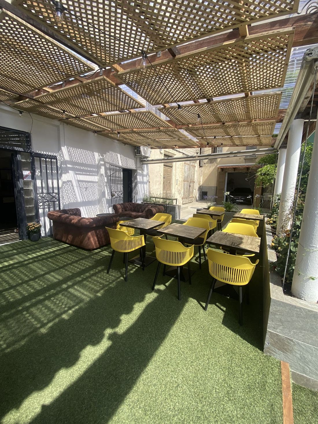 Terrasse couverte sous pergola avec canapé Chesterfield et chaises jaunes.