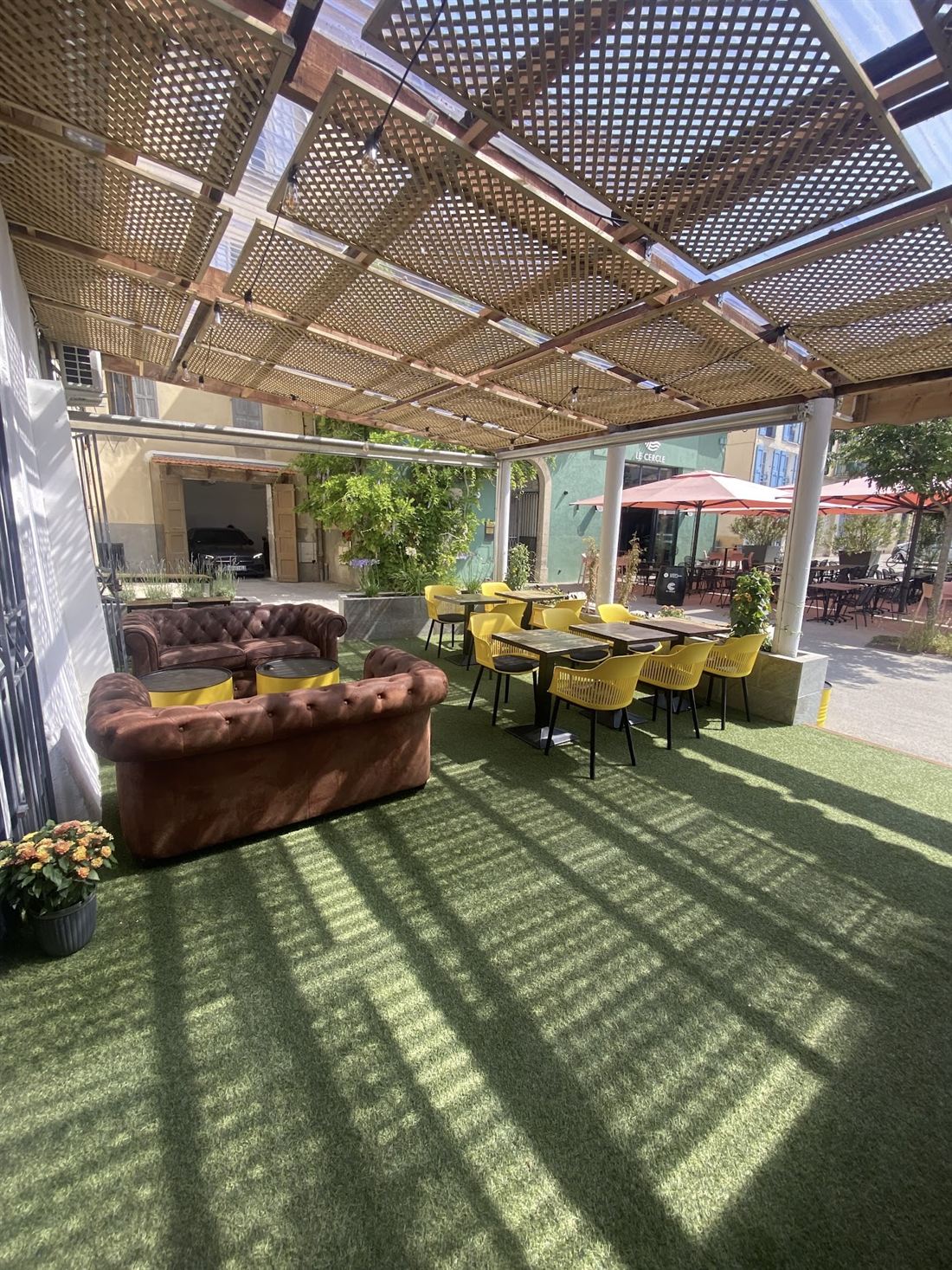 Terrasse couverte sous pergola en lattes, canapé Chesterfield et chaises jaunes.